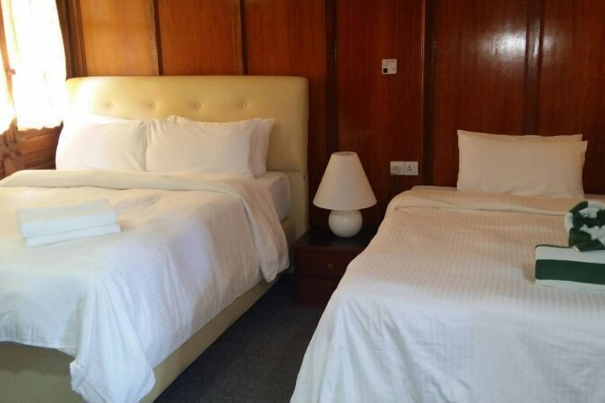 Une chambre d’hôtel avec deux lits, chacun étant équipé de draps et d’oreillers blancs. Une table de chevet avec une lampe se trouve entre les deux lits.