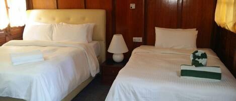 A hotel room with two beds, each with white linens and pillows. There is a bedside table with a lamp between the beds.