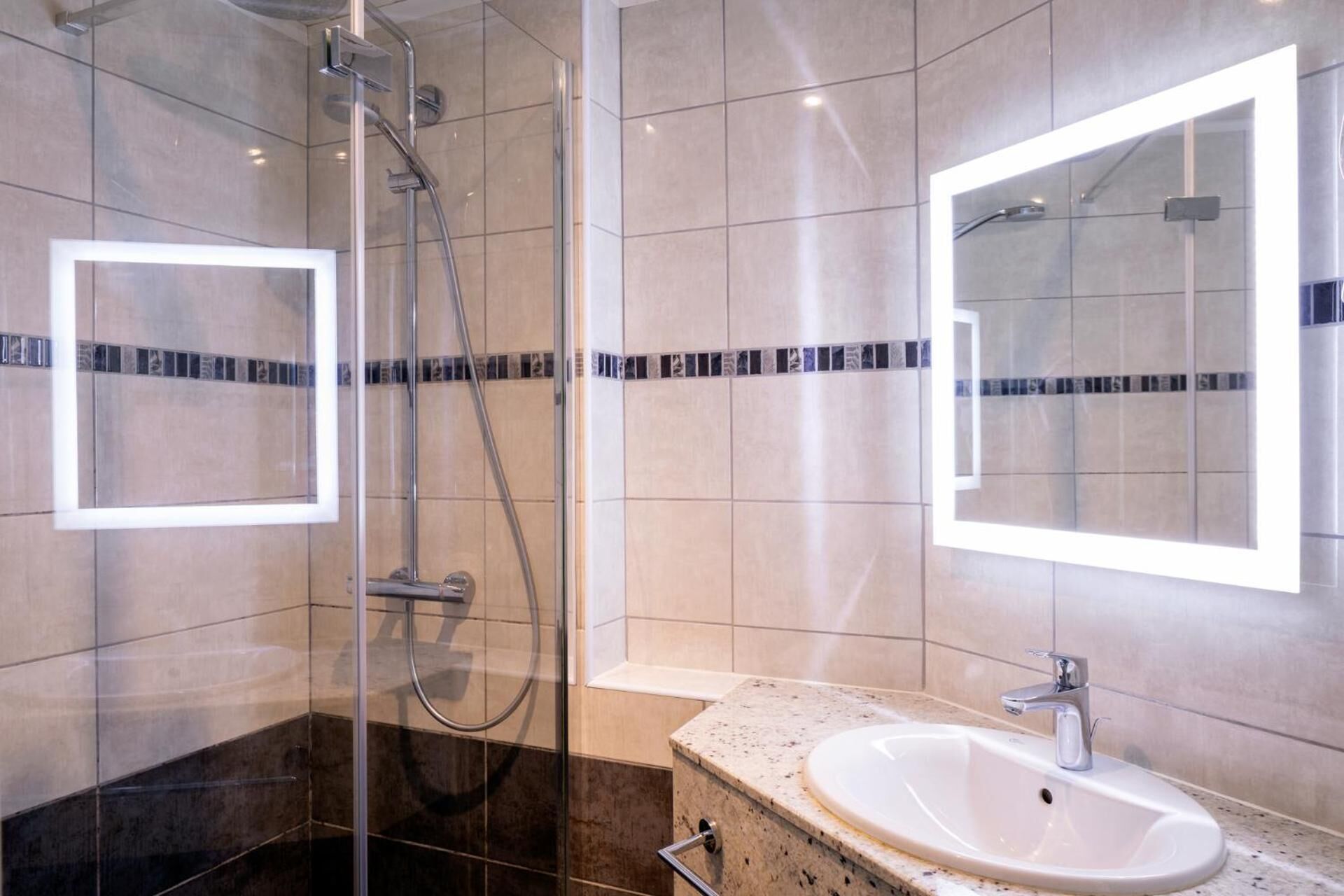 A modern bathroom with a glass-enclosed shower, a sink with a marble countertop, and mirrored walls.