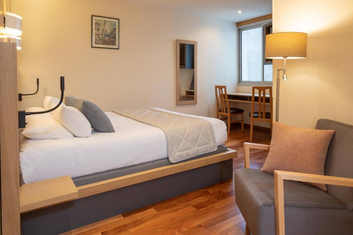 A bedroom with a bed, bedside table, lamp, and a view of a dining area.