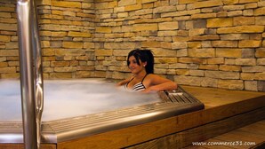 A woman in a stone-walled hot tub with a wooden bench.
