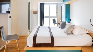 A modern hotel room with a large bed, a desk, and a TV.