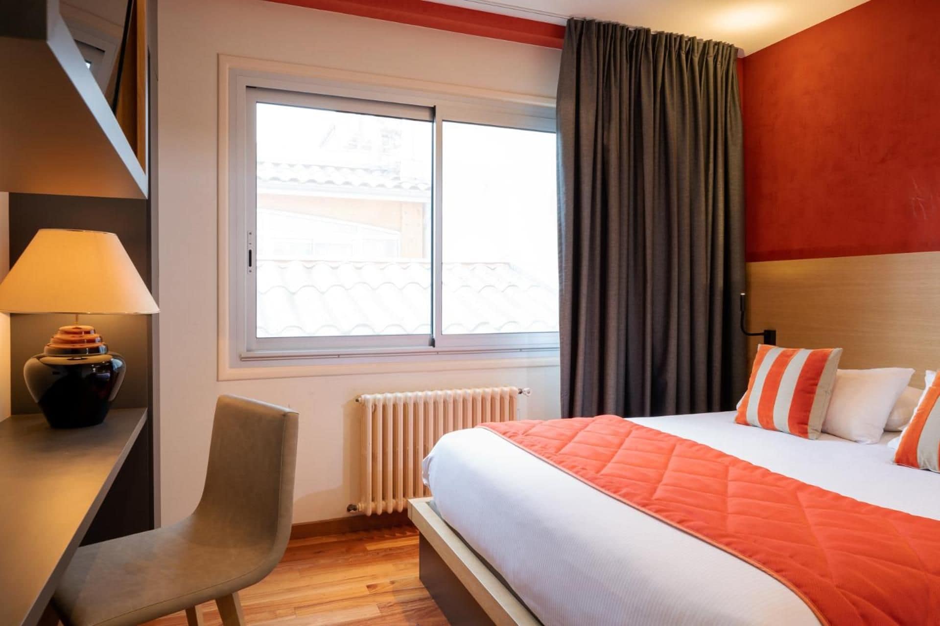 Habitación de hotel con cama, escritorio, silla, ventana con cortinas y radiador.