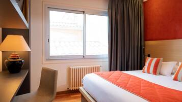 Habitación de hotel con cama, escritorio, silla, ventana con cortinas y radiador.