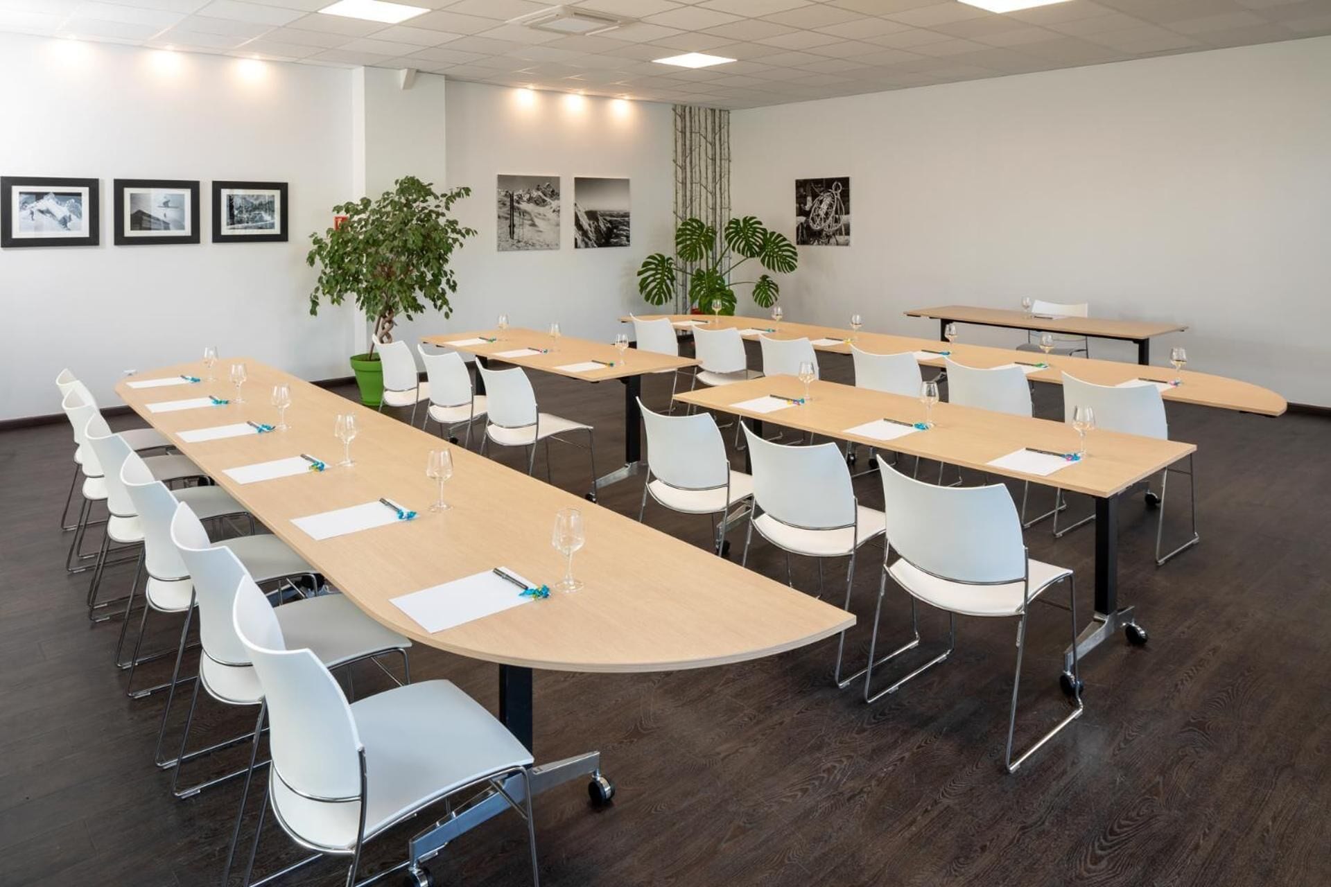 A conference room with long tables, white chairs, and framed pictures on the walls.