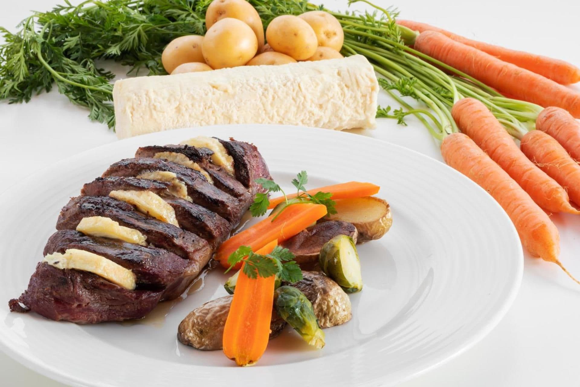 A plate with sliced meat, carrots, and Brussels sprouts.