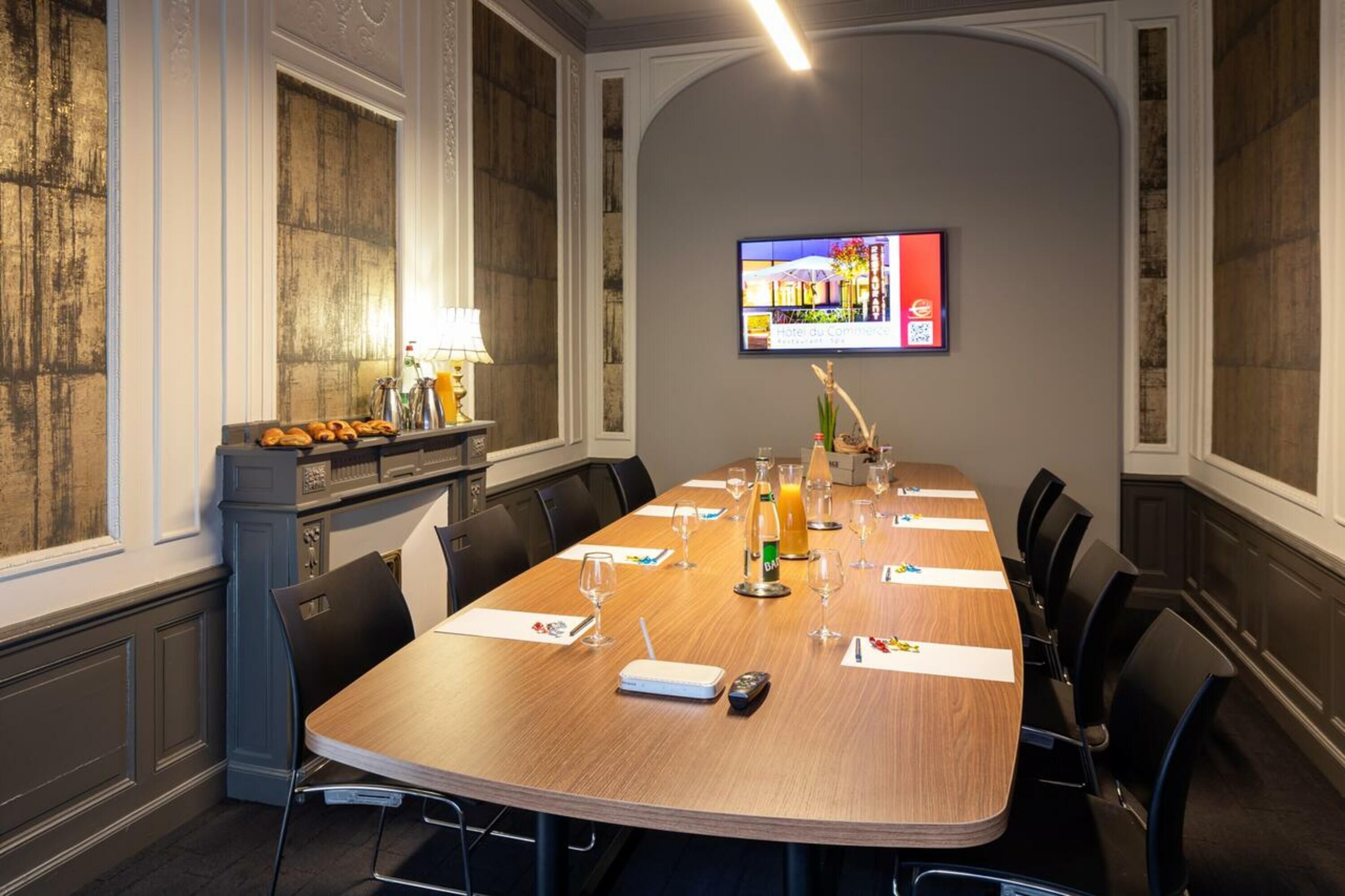 Un salón de conferencias con una larga mesa, sillas, una pantalla de televisión y una zona de bufé con pasteles.