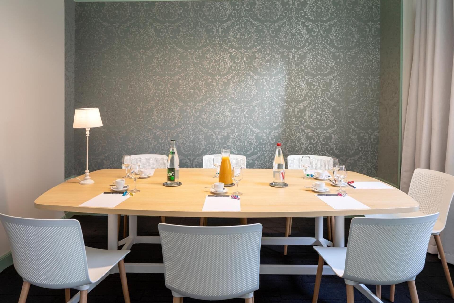 A conference room with a round table, six chairs, a lamp, and various beverages.
