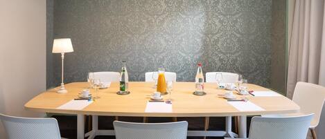 Un salón de conferencias con una mesa redonda, seis sillas, una lámpara y diversas bebidas.