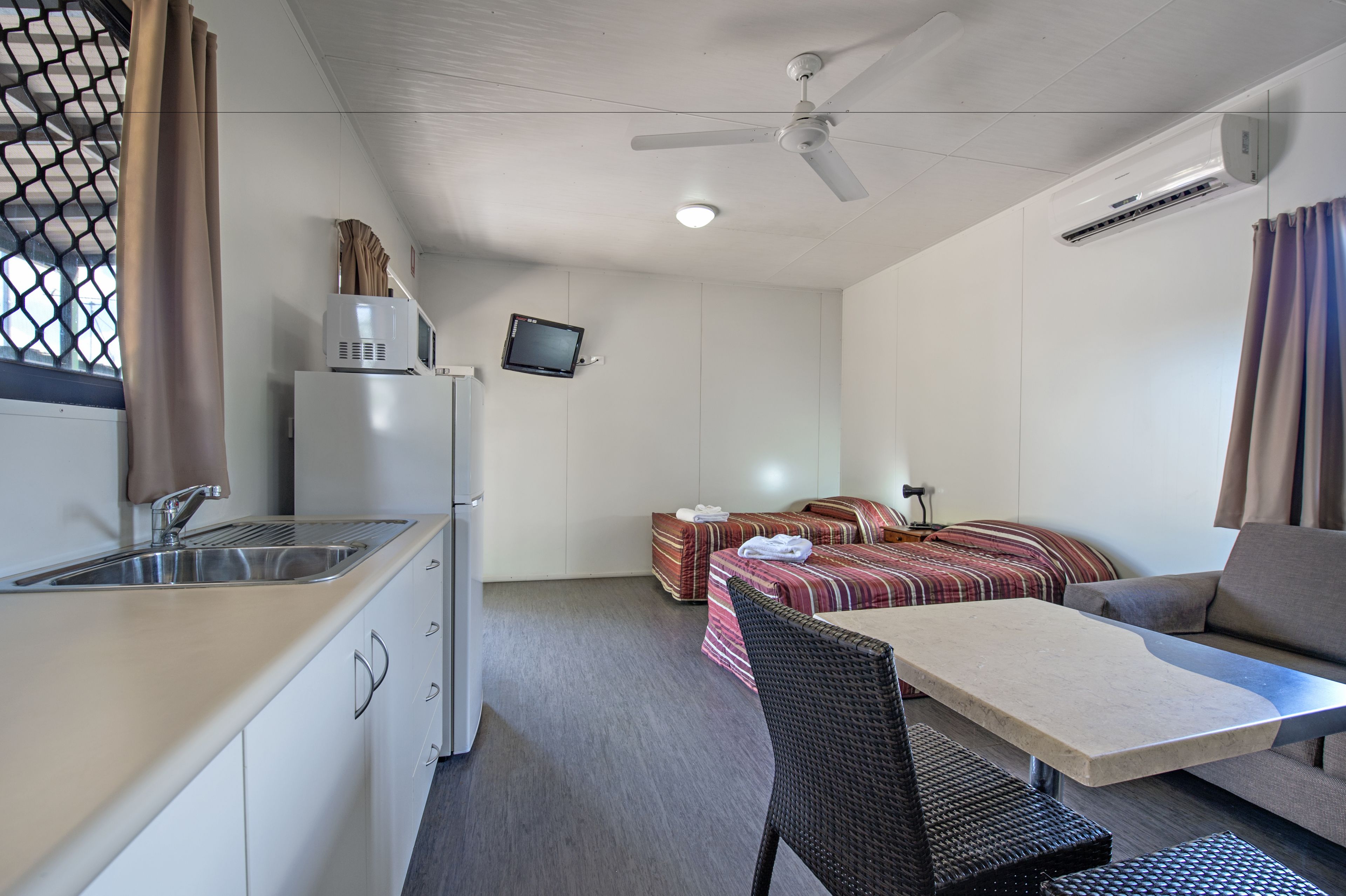 A compact room with a kitchenette, a bed with a striped blanket, a small table, and a ceiling fan.