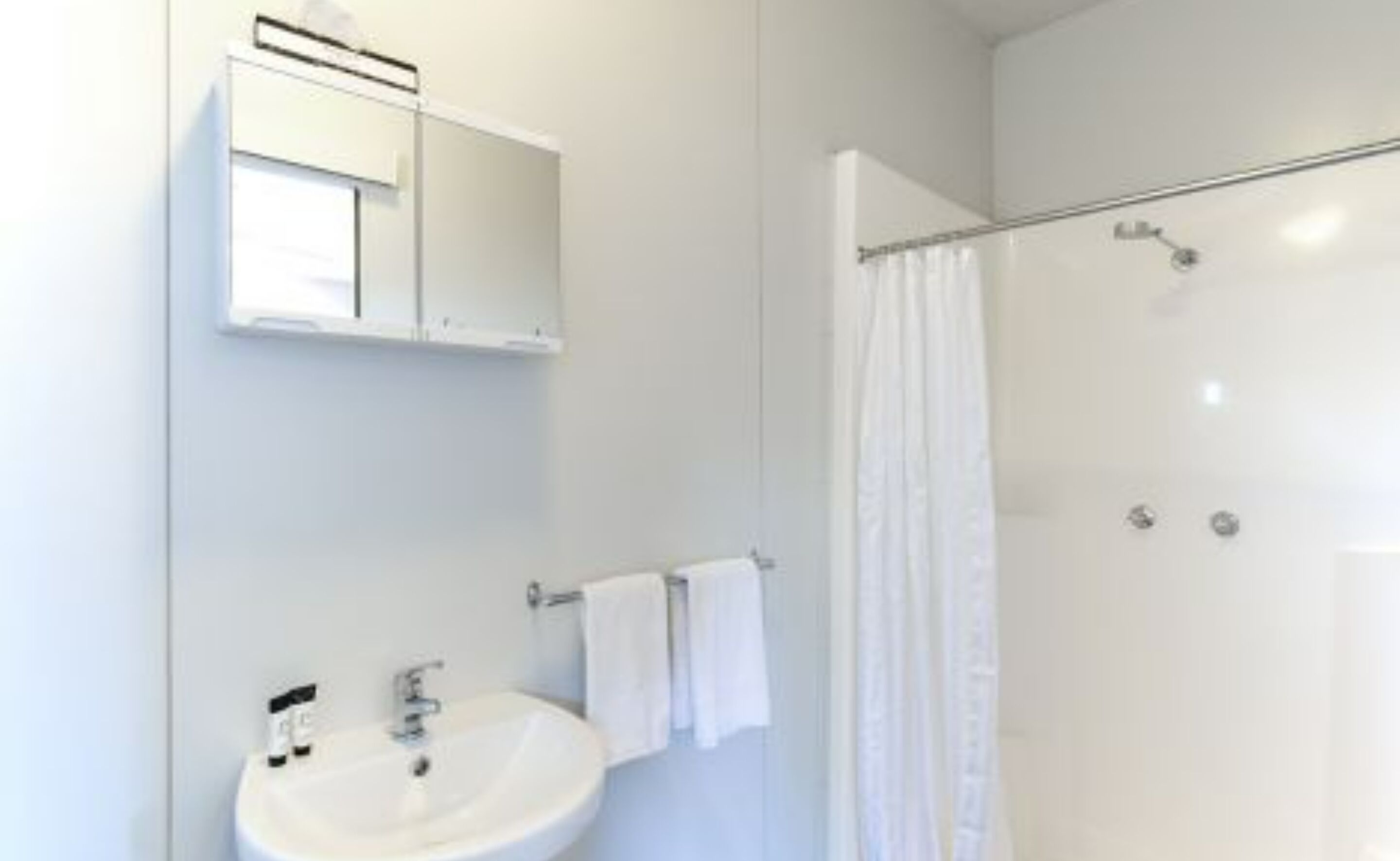 Ein modernes Badezimmer mit einem weißen Waschbecken, einem Spiegel und einer Duschkabine.