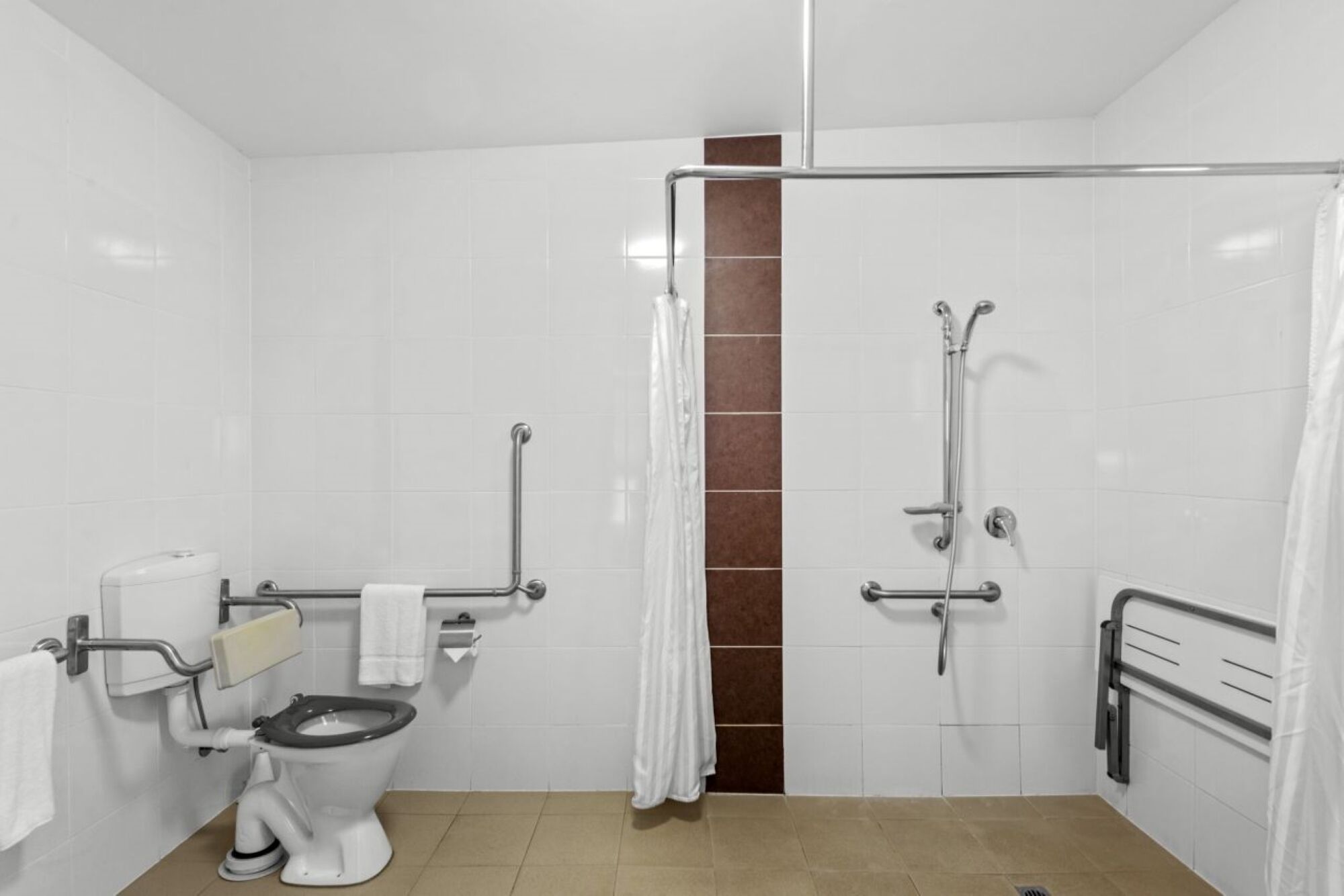 Ein Badezimmer mit Toilette, Haltegriffen, einer Dusche mit Glastür und einem Handtuchhalter.