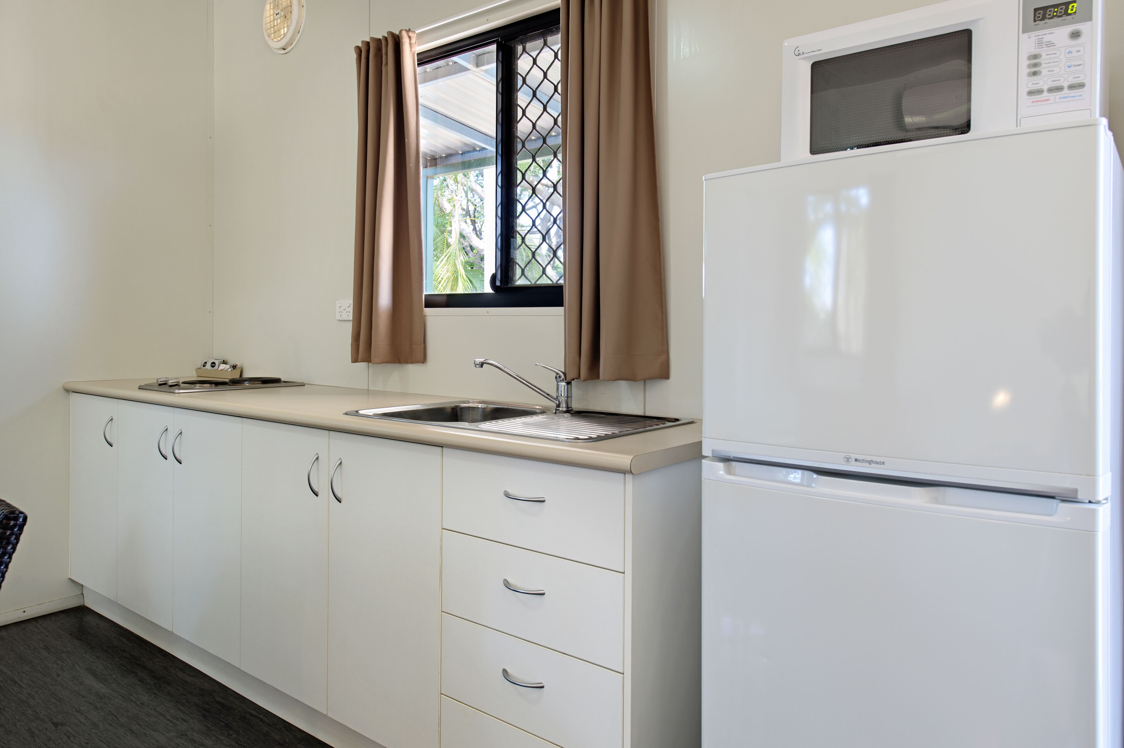 A kitchen with white cabinets, a sink, a window with curtains, and a white refrigerator.
