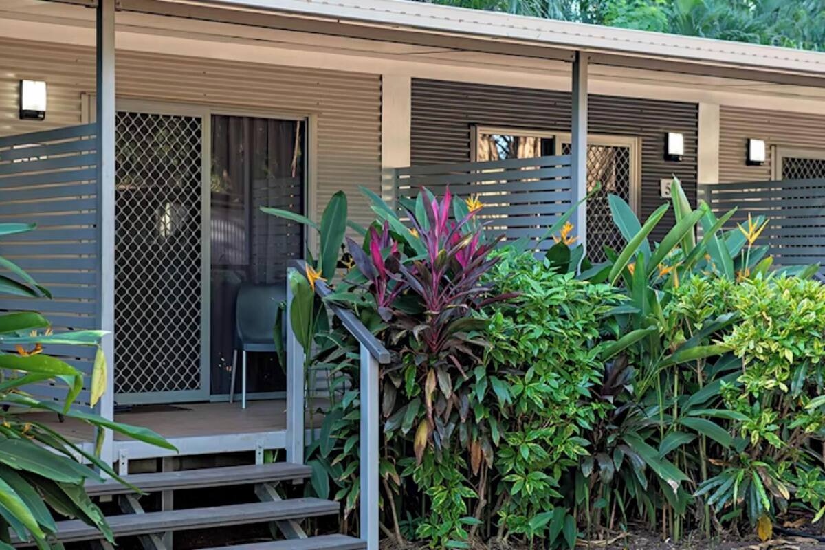 A modern hotel with a covered outdoor area, numbered rooms, and lush tropical plants.