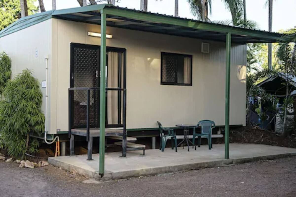 A small, single-story building with a covered porch, a bench, and two chairs.