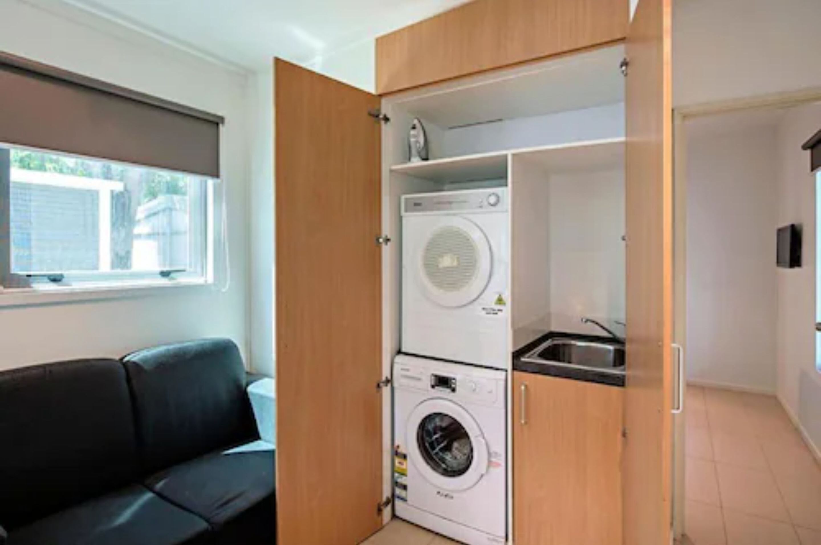 Une petite buanderie comprenant un lave-linge et un sèche-linge, un petit évier et un canapé noir.