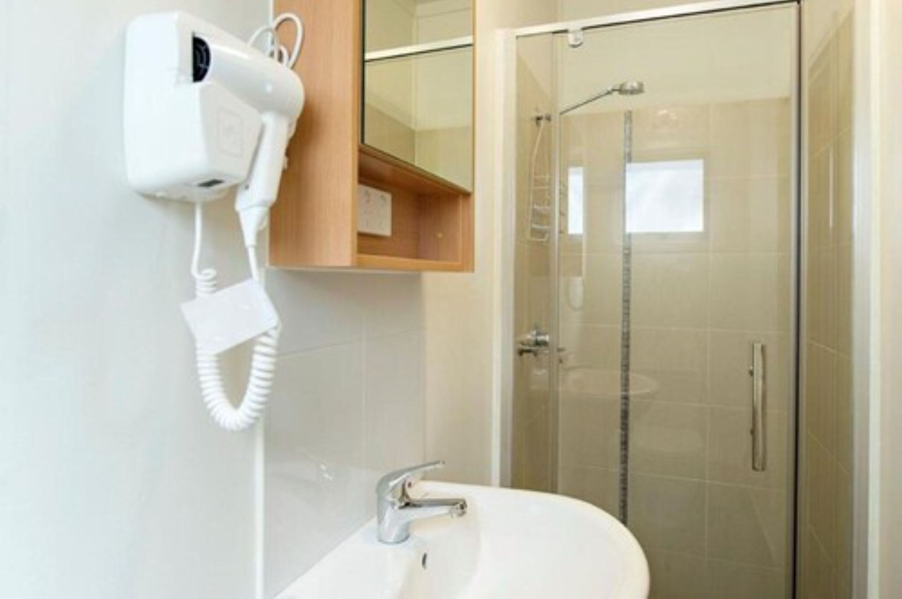 A bathroom with a white sink, a hairdryer mounted on the wall, and a glass-enclosed shower.