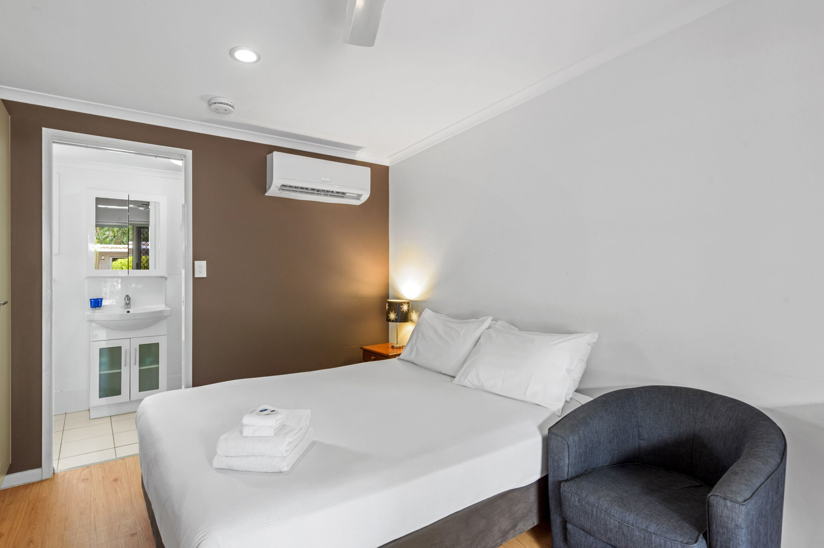 Een hotelkamer met een bed, nachtkastje, lamp en een stoel.
