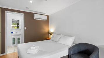 Een hotelkamer met een bed, nachtkastje, lamp en een stoel.