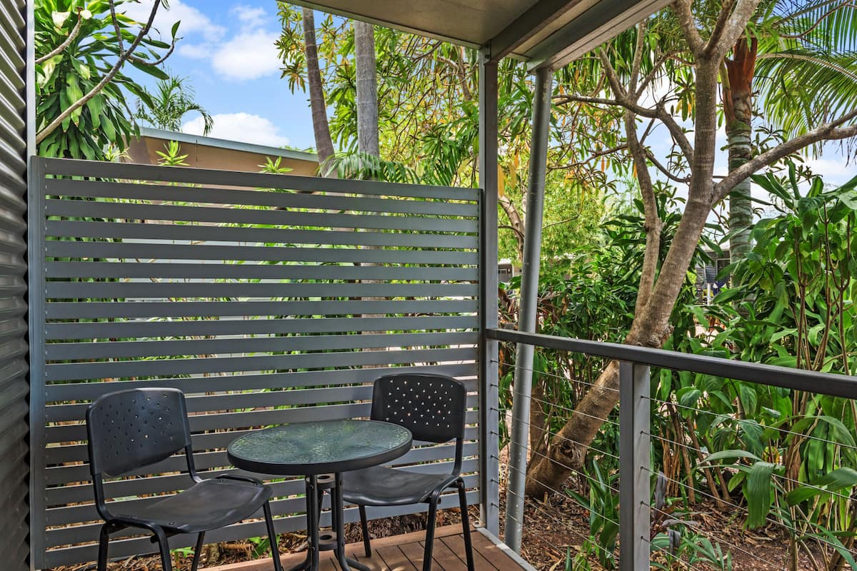 A balcony with two black chairs and a small round table, surrounded by a metal railing and lush greenery.