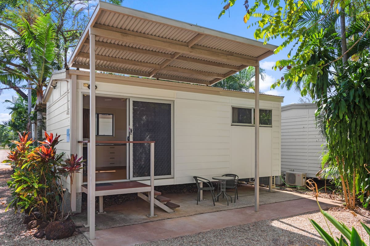A small, single-story mobile home with a covered porch, a sliding door, and a small patio area with a table and chairs.