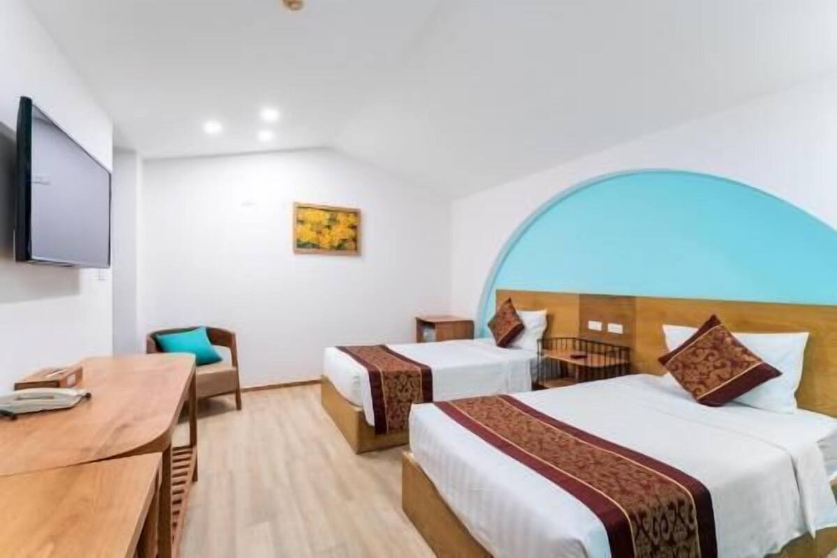 A hotel room with two beds, a desk, a chair, a TV, and a painting on the wall.