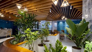 A modern reception area with wooden ceiling beams, potted plants, and a curved reception desk. - Prime Hotel (Nha Trang)