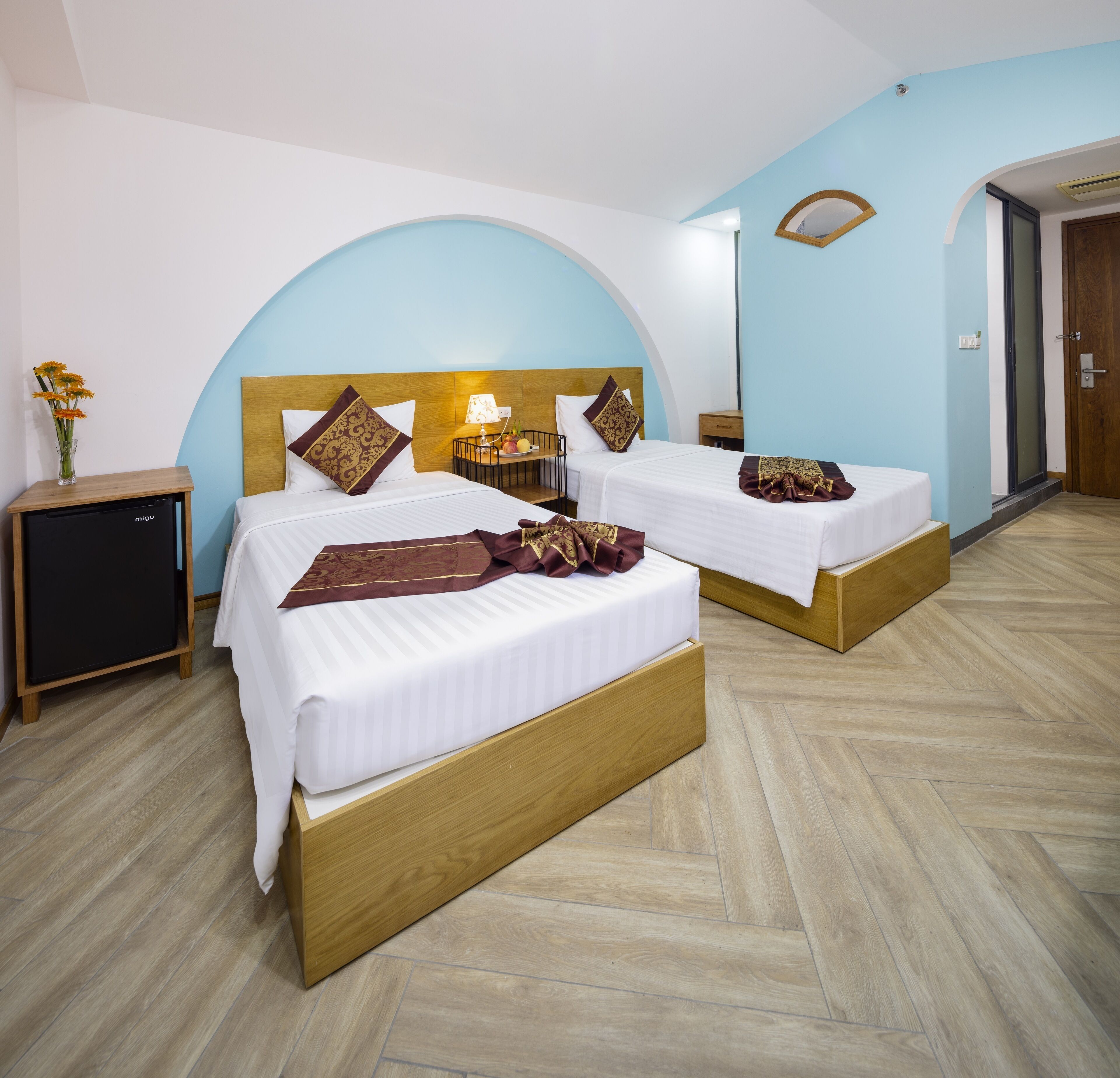 Habitación de hotel con dos camas, una mesita de noche, una lámpara y un armario pequeño.