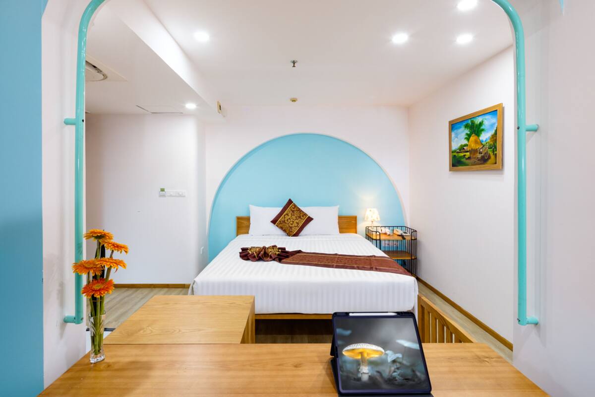 A modern hotel room with a bed, a bedside table, a vase with flowers, and a painting on the wall.