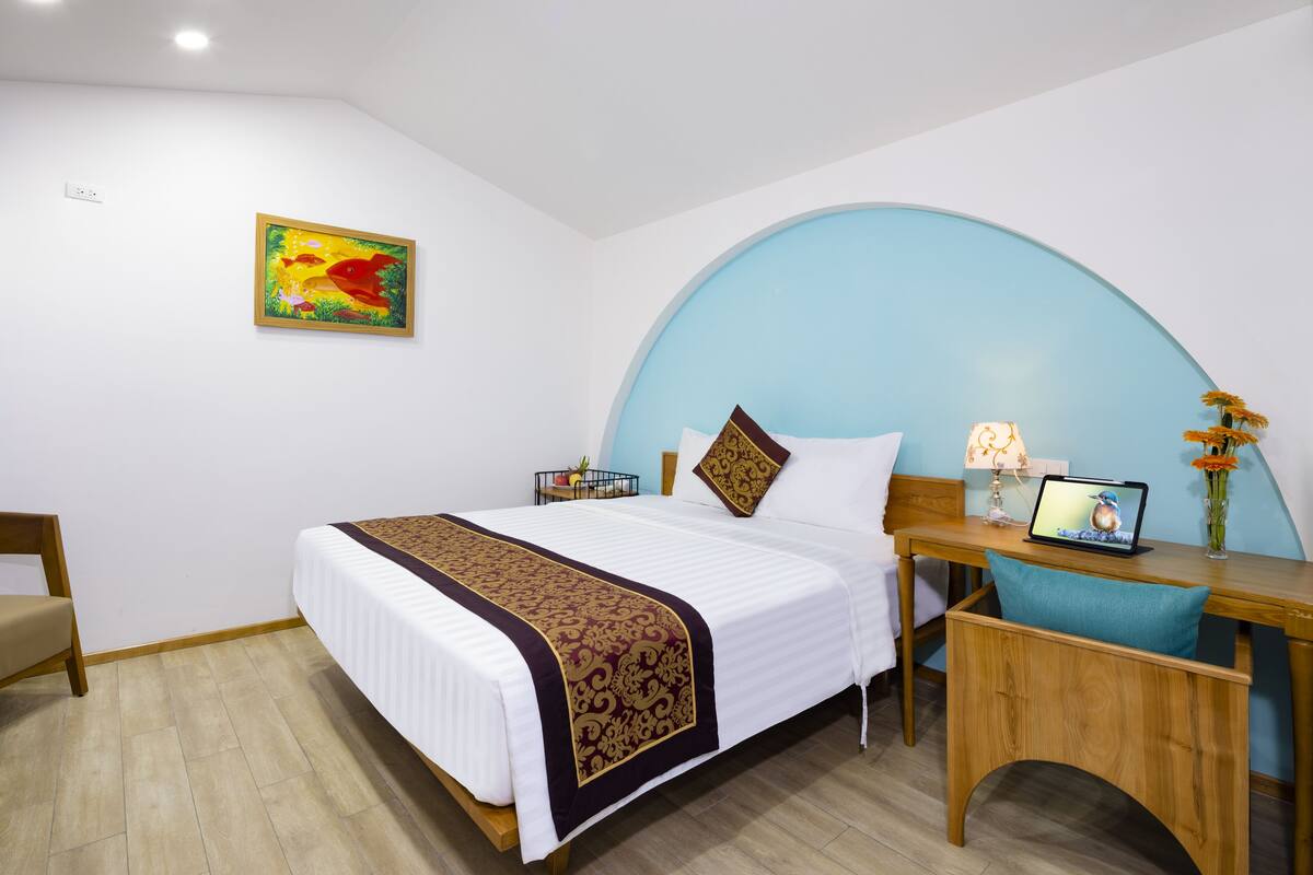 A hotel room with a bed, desk, chair, and a wall-mounted TV.