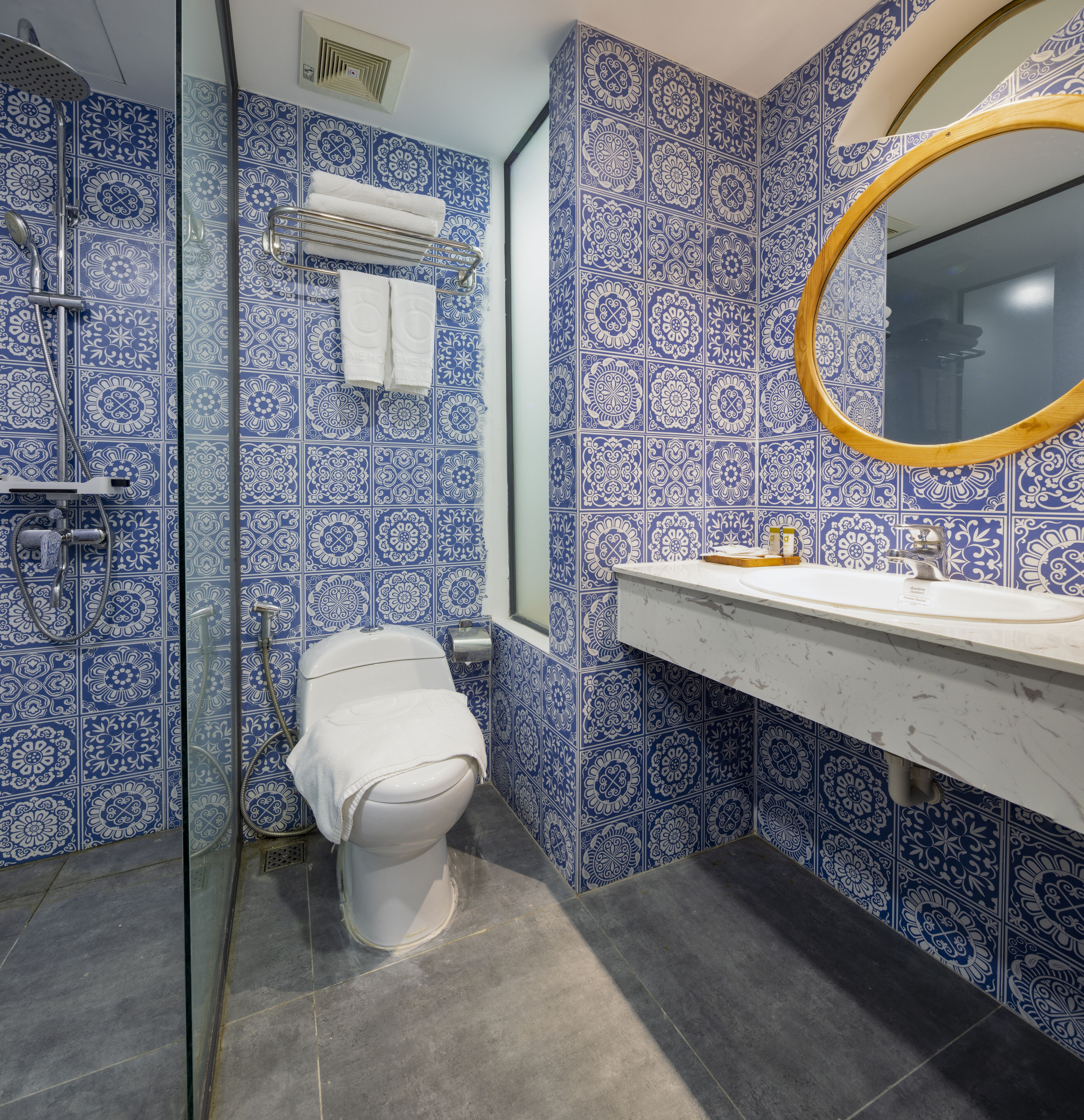 Een badkamer met blauwe betegelde wanden, een wit toilet, een glazen douchecabine en een witte wastafel met een spiegel met houten lijst.