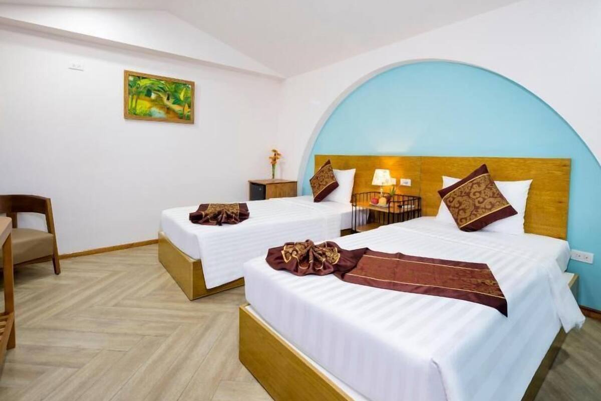 A hotel room with two beds, a wooden headboard, a small table with a lamp, and a chair.