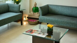 Un salon moderne avec deux canapés gris, une table basse en verre, une statue de Bouddha et un vase rempli de fleurs jaunes.
