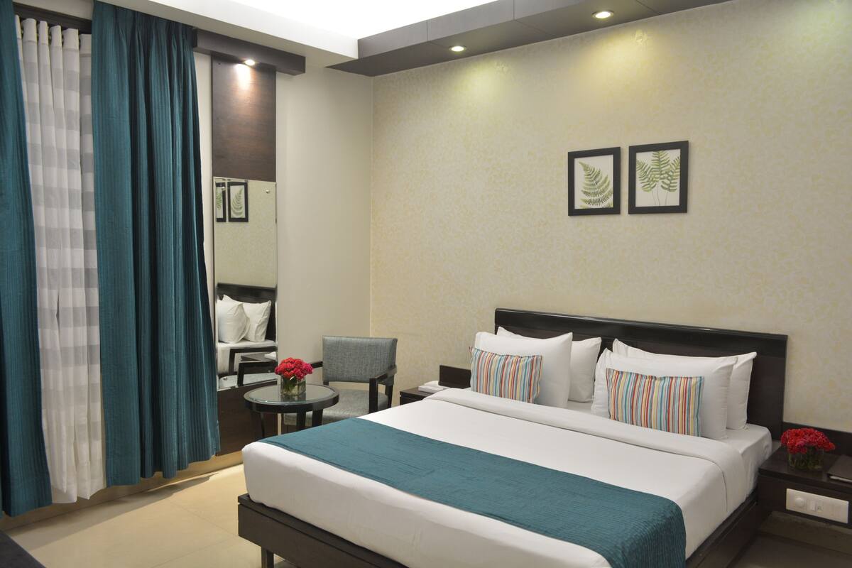 Quarto de hotel com uma cama grande, uma cadeira, uma mesinha com um vaso de flores e uma mesa de cabeceira com abajur.
