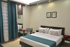 A hotel room with a large bed, a chair, a small table with a vase of flowers, and a nightstand with a lamp. - Rockland Hotel Panchsheel Enclave (New Delhi)