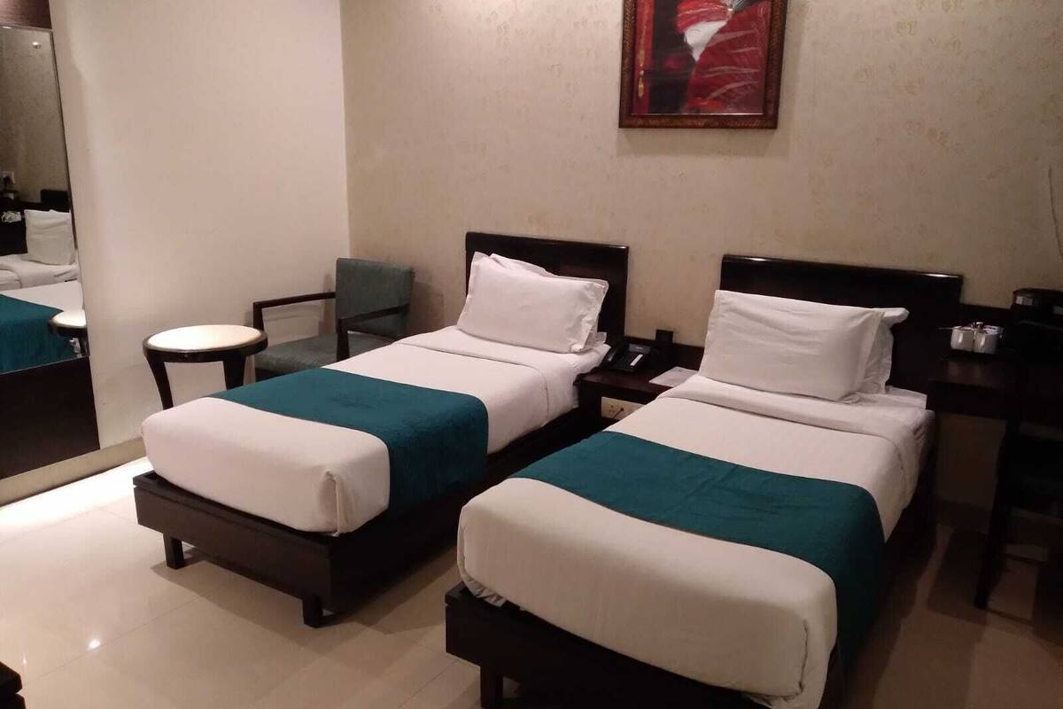 Quarto de hotel com duas camas, uma mesinha redonda, uma cadeira e um quadro na parede.