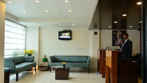 Un hall d’entrée moderne avec un canapé, une table basse, un téléviseur fixé au mur et une rangée de pupitres en bois.