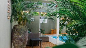 A covered outdoor area with a wooden deck, a large planter, wicker furniture, and a sign indicating a depth of 1 meter. - The Cooks Oasis (Rarotonga)