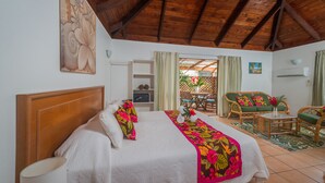 A hotel room with a wooden ceiling, a bed with floral bedding, a green sofa, and a dining area with a table and chairs. - The Cooks Oasis (Rarotonga)