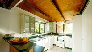 A kitchen with white cabinets, a wooden countertop, and a window with a view of greenery. - The Cooks Oasis (Rarotonga)