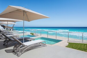A poolside area with lounge chairs and umbrellas overlooking a beach with waves.