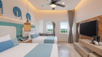 Habitación de hotel con dos camas, televisión, escritorio y vista al mar.