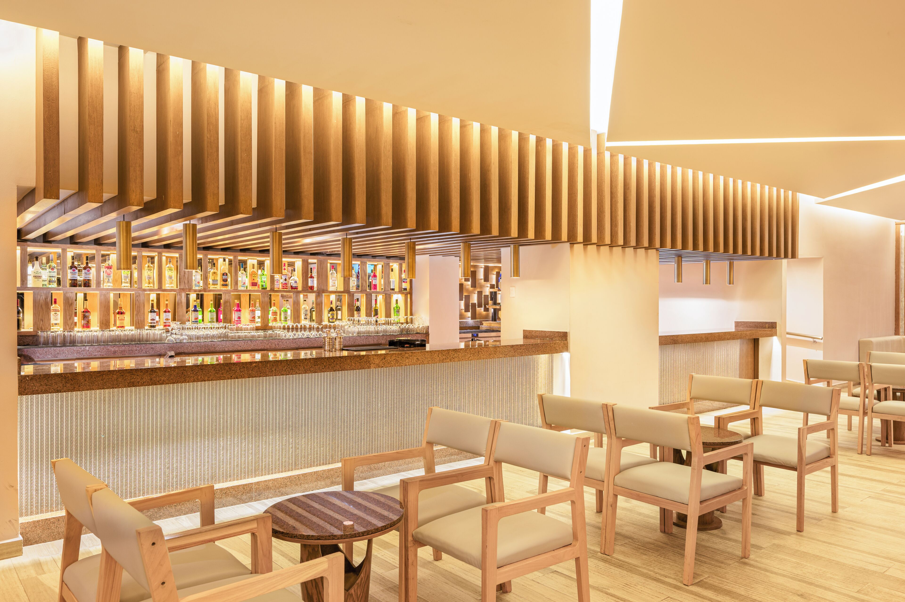 Un espacio moderno de bar con paneles de madera, diversas botellas de licor y diferentes disposiciones de asientos.