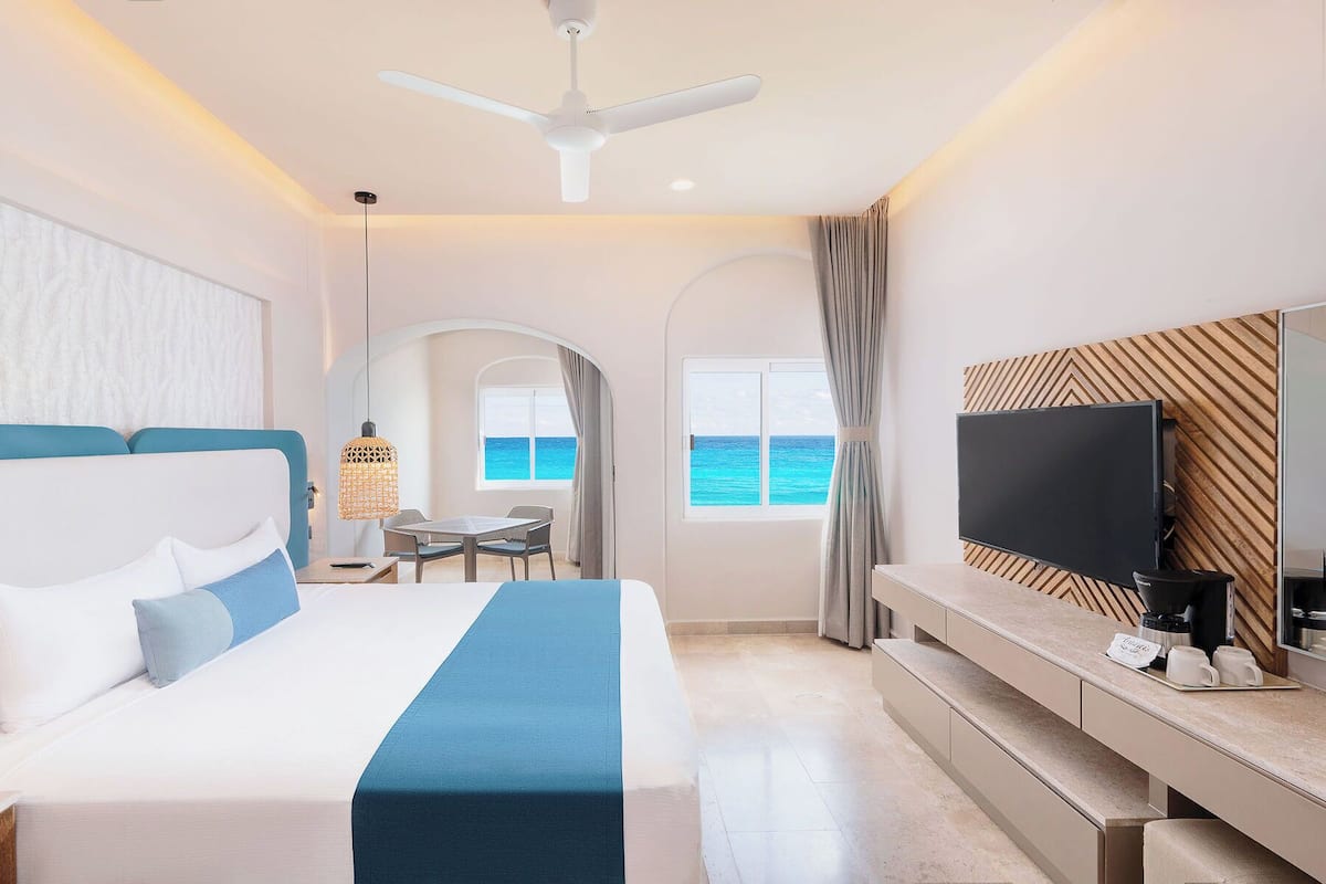 A modern hotel room with a large bed, a TV, and a view of the ocean.