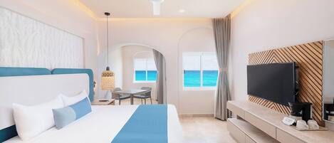 A modern hotel room with a large bed, a TV, and a view of the ocean.