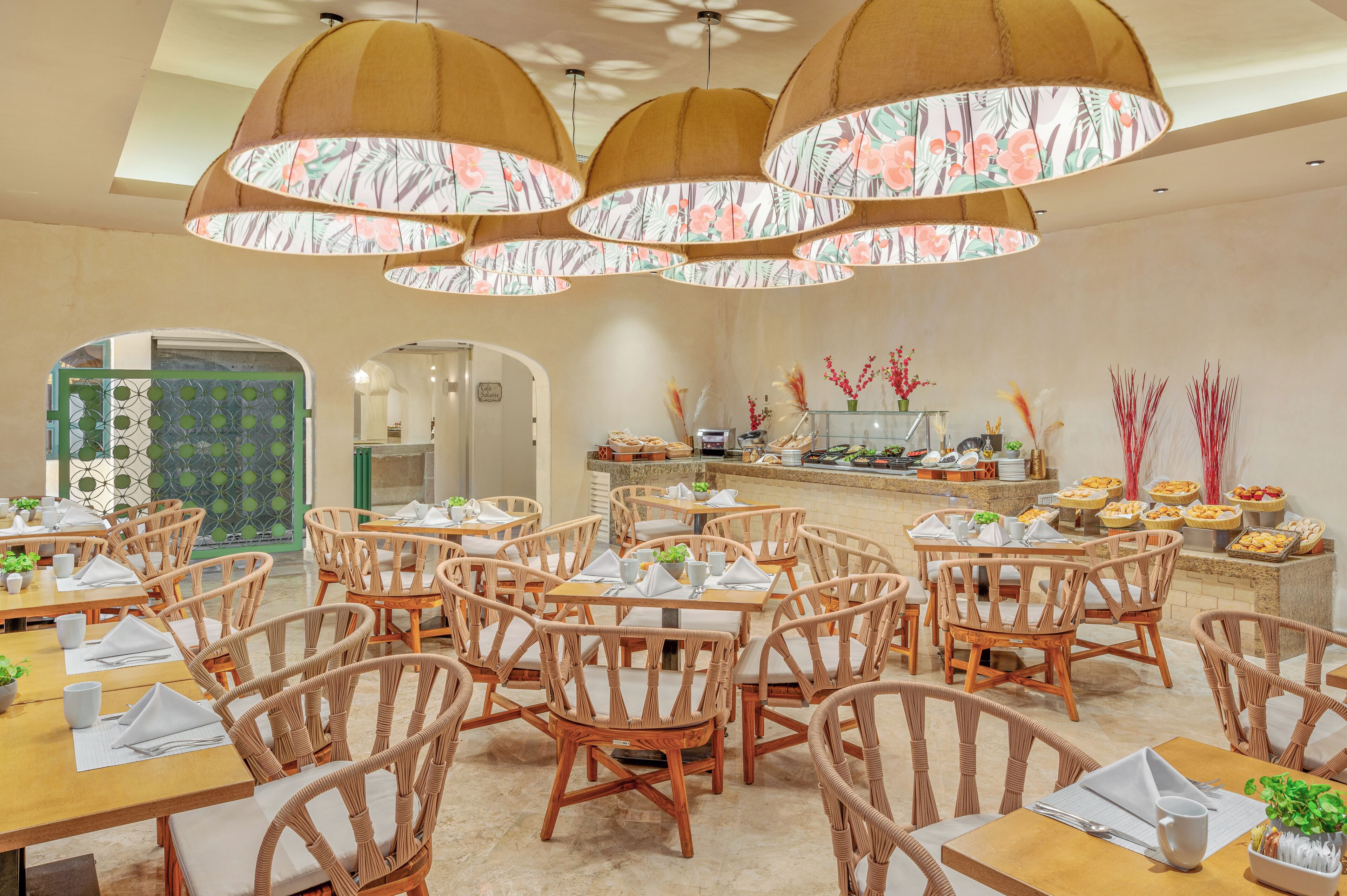 A dining area with wicker chairs and tables, a buffet with various food items, and a floral-patterned ceiling light fixture.