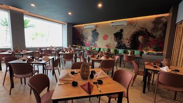 A restaurant with multiple tables and chairs, large windows, and a mural on the wall.