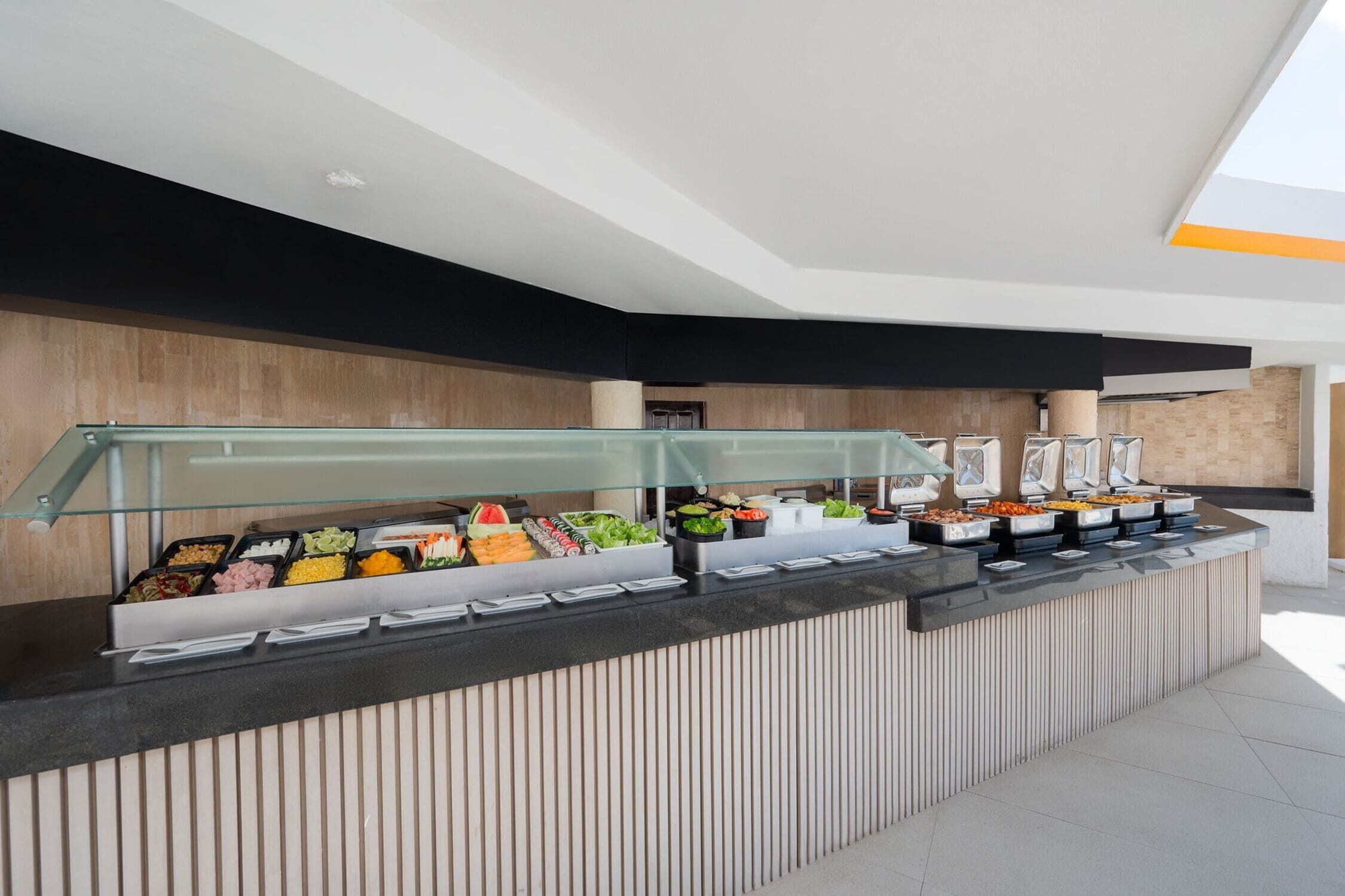 A buffet area with various food options, a modern design with a glass partition, and a wooden accent wall.