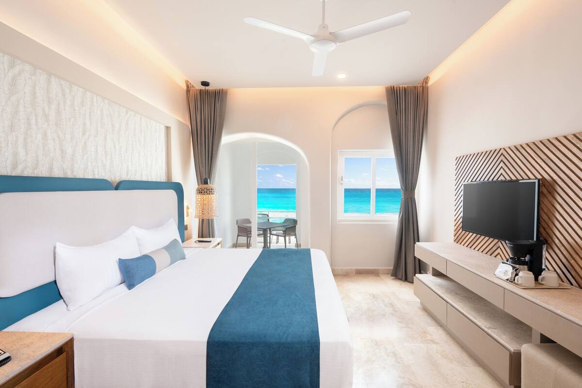 A hotel room with a bed, a TV, a desk, and a view of the ocean.