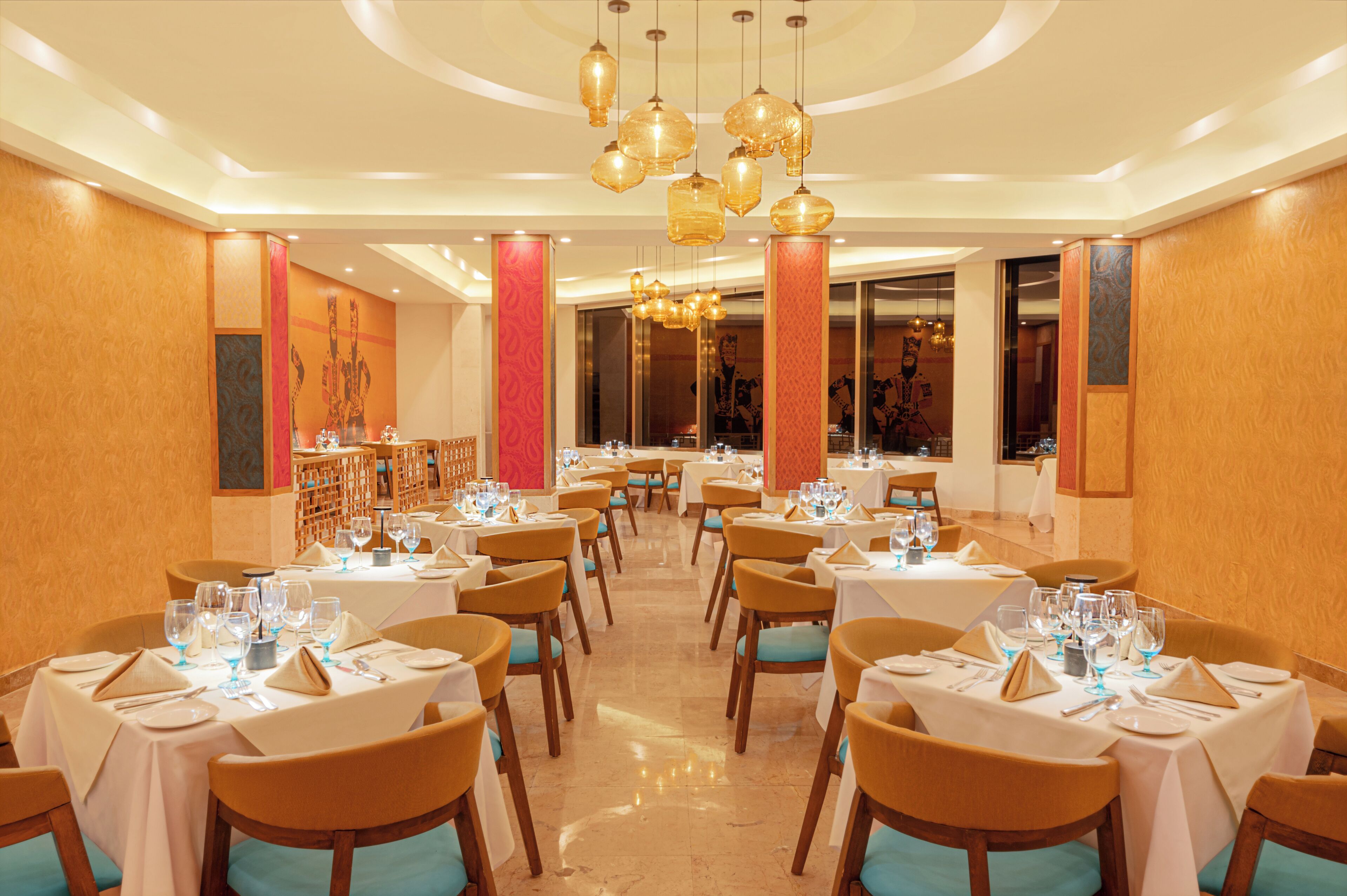 A dining area with multiple tables set for service, featuring a central chandelier and a warm color scheme.